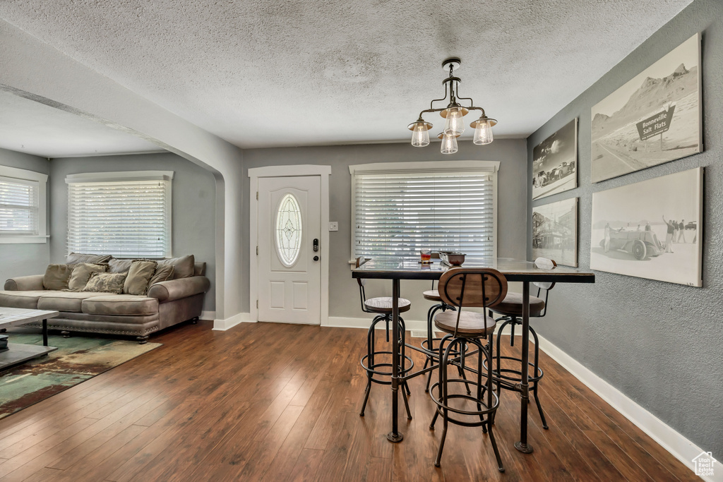 Dining room with dark wood-style floors, a textured ceiling, baseboards, arched walkways, and a chandelier