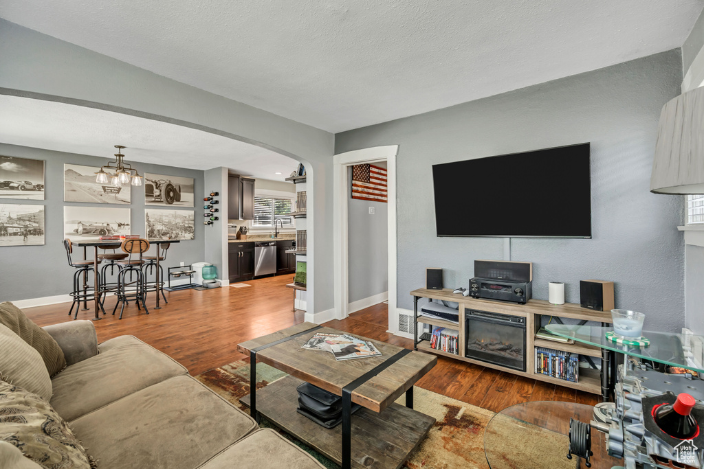 Living area featuring wood finished floors, arched walkways, a chandelier, and baseboards