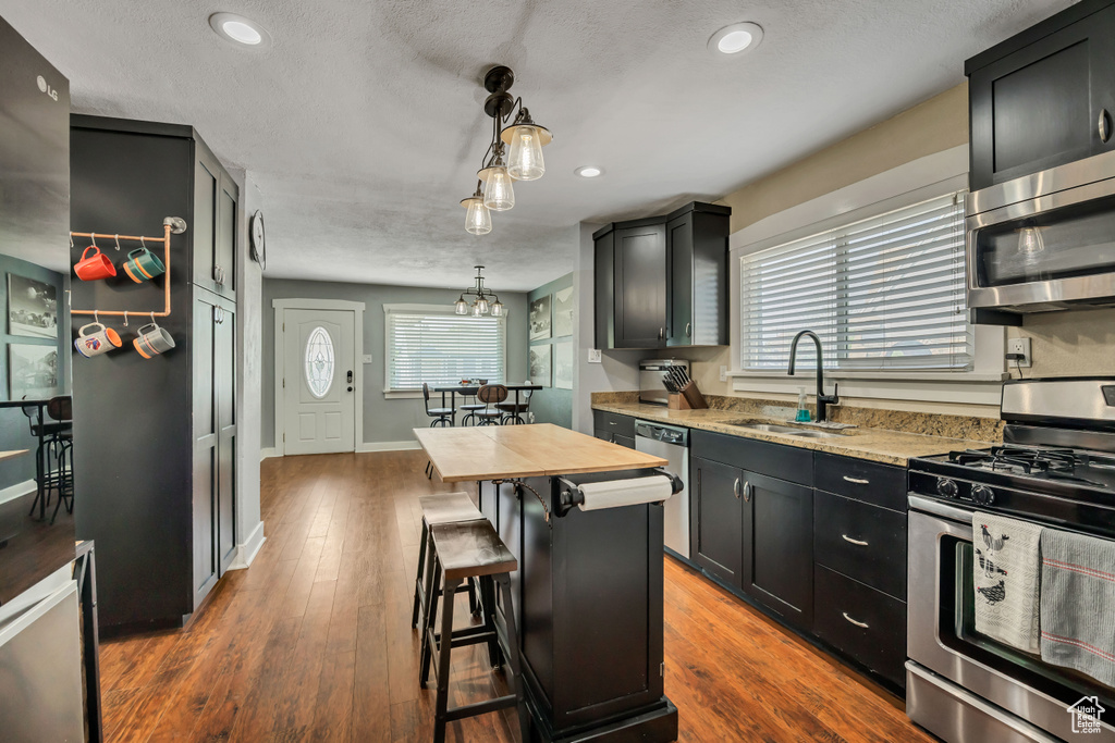 Kitchen featuring stainless steel appliances, a sink, recessed lighting, a kitchen bar, and dark wood-type flooring