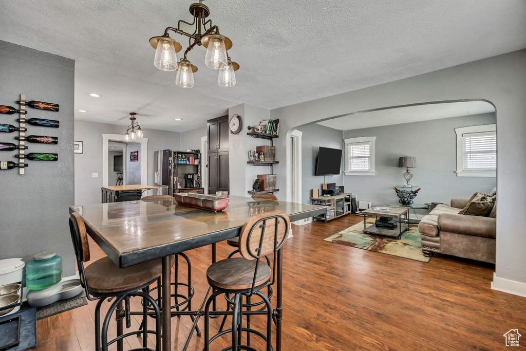 Dining room featuring arched walkways, wood finished floors, a textured ceiling, baseboards, and a chandelier