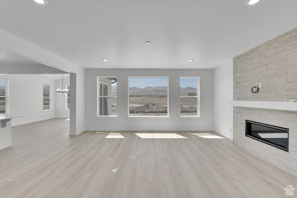 Unfurnished living room featuring a fireplace, a chandelier, baseboards, light wood-style floors, and recessed lighting
