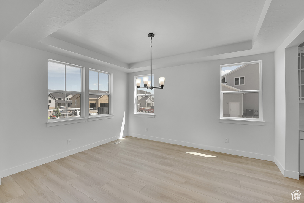 Unfurnished dining area with a tray ceiling, a chandelier, light wood finished floors, and baseboards