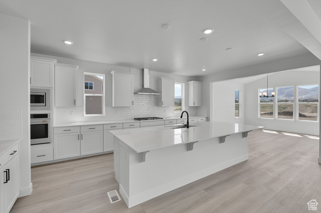 Kitchen with appliances with stainless steel finishes, wall chimney range hood, a sink, a chandelier, and a breakfast bar area