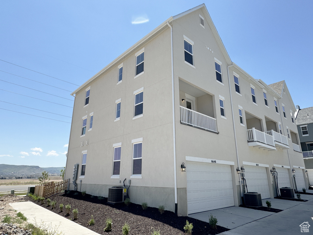 View of building exterior featuring cooling unit, an attached garage, and concrete driveway