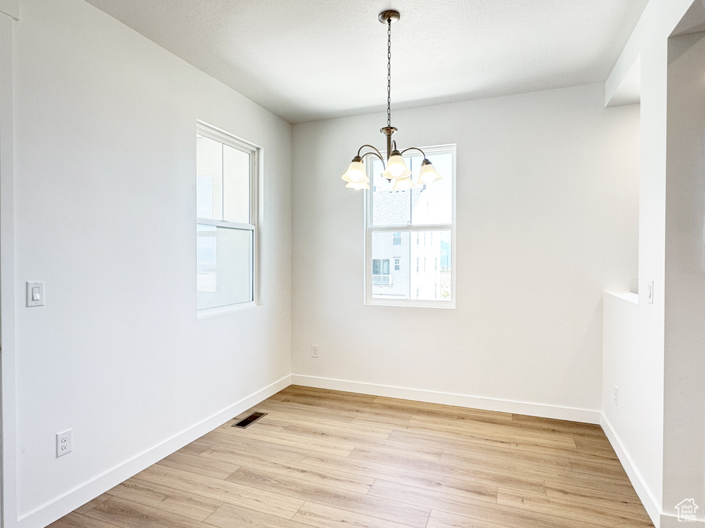 Unfurnished room with plenty of natural light, a chandelier, light wood-style flooring, and baseboards