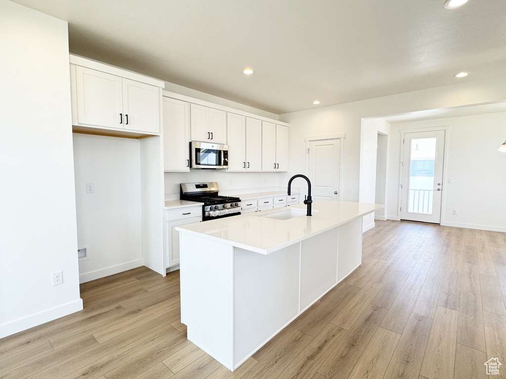 Kitchen with appliances with stainless steel finishes, a sink, light wood-type flooring, white cabinetry, and an island with sink