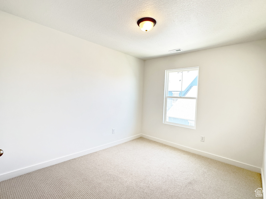 Spare room with light carpet, baseboards, and a textured ceiling