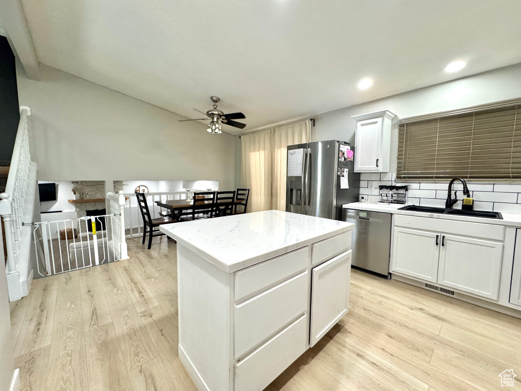 Kitchen with appliances with stainless steel finishes, a sink, ceiling fan, light wood finished floors, and white cabinetry
