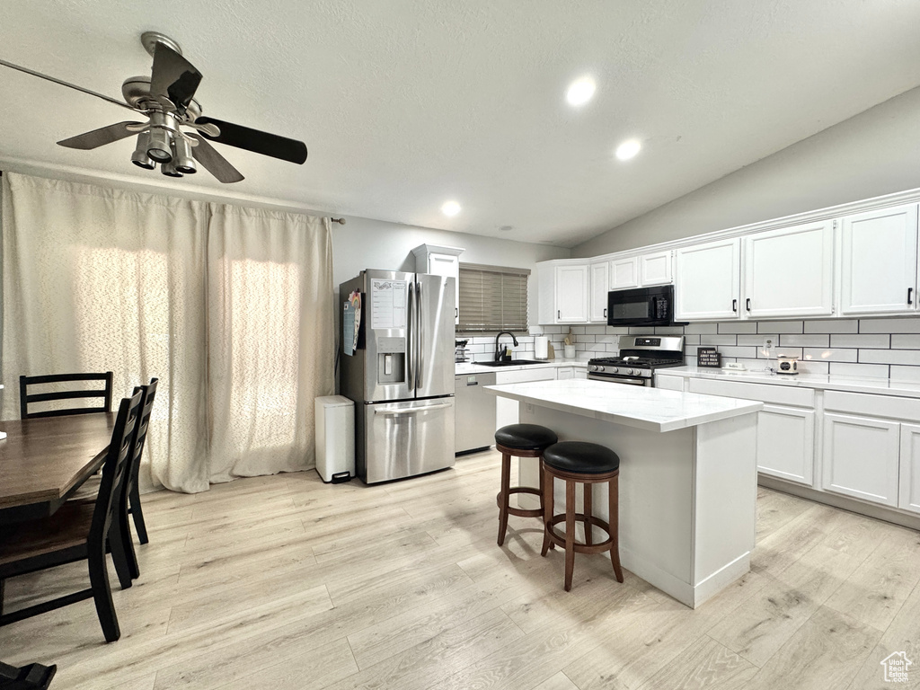 Kitchen with stainless steel appliances, light wood finished floors, a kitchen island, light countertops, and white cabinetry