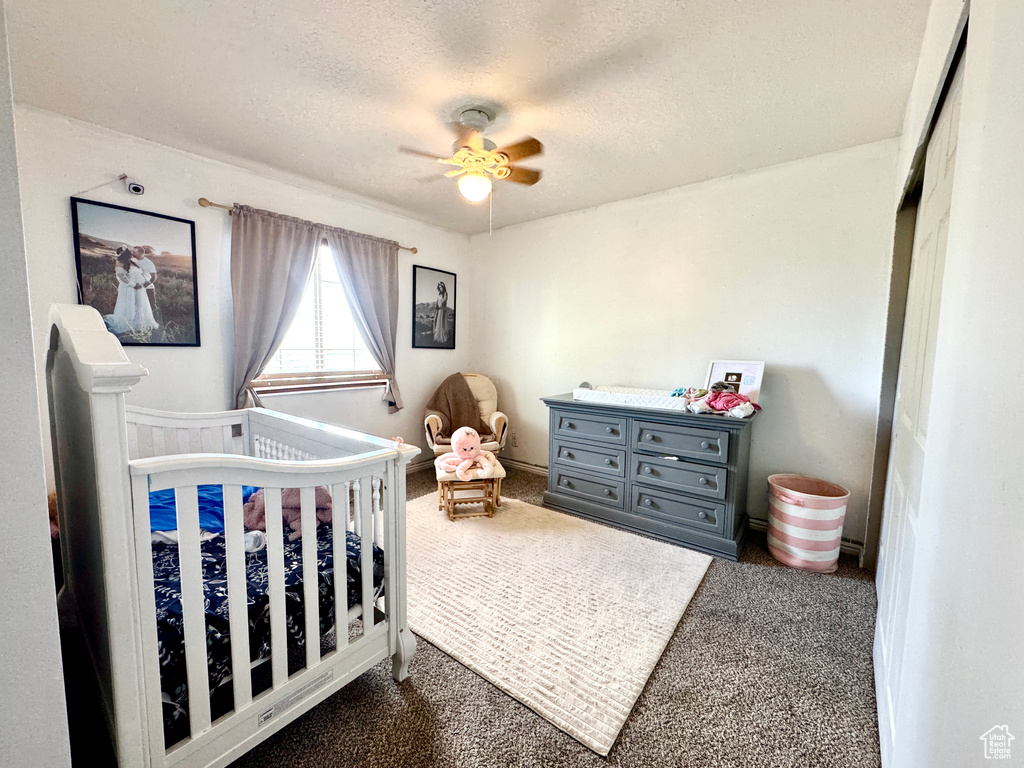 Bedroom featuring dark colored carpet, a textured ceiling, a nursery area, and ceiling fan