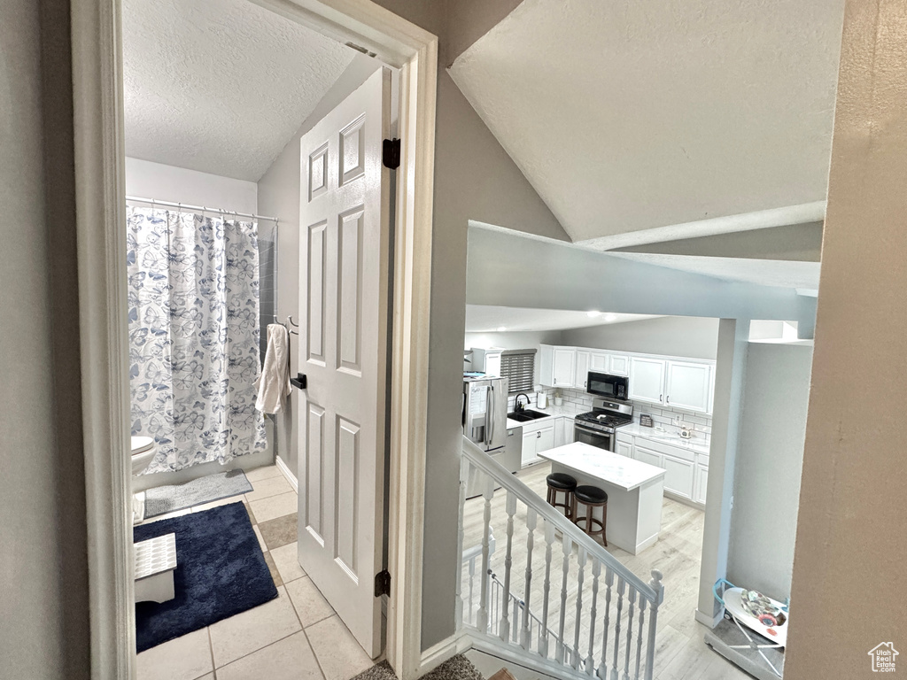 Bathroom featuring a sink, a textured ceiling, toilet, tile patterned floors, and vaulted ceiling