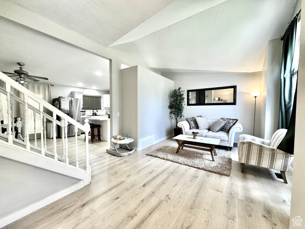 Living room with light wood-style floors, lofted ceiling, a ceiling fan, baseboards, and stairway