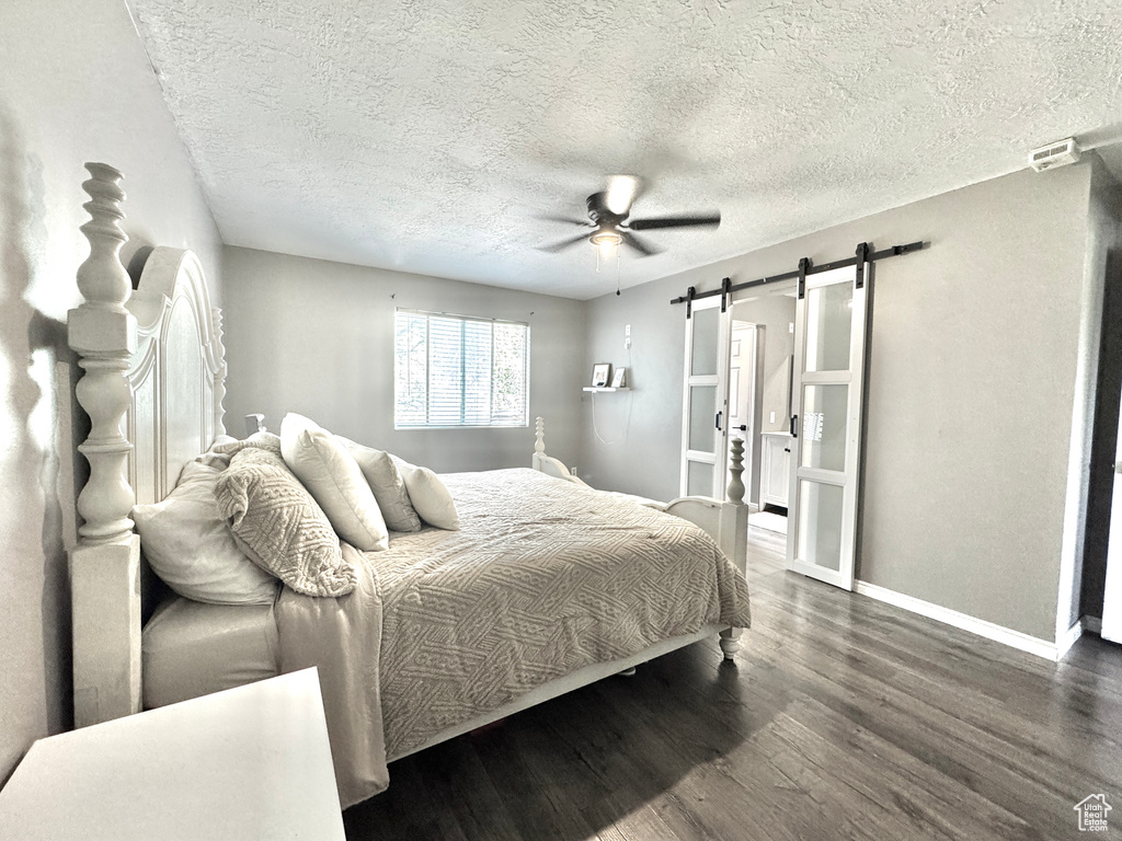 Bedroom with a barn door, wood finished floors, baseboards, a textured ceiling, and a ceiling fan