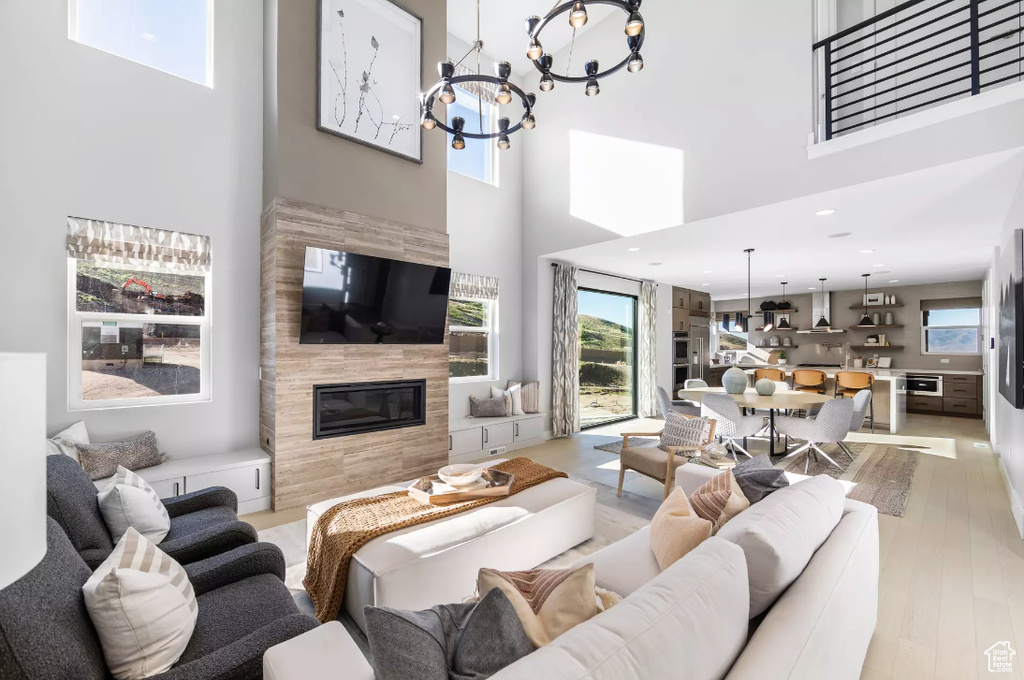 Living room with a towering ceiling, a chandelier, a tile fireplace, and light wood finished floors