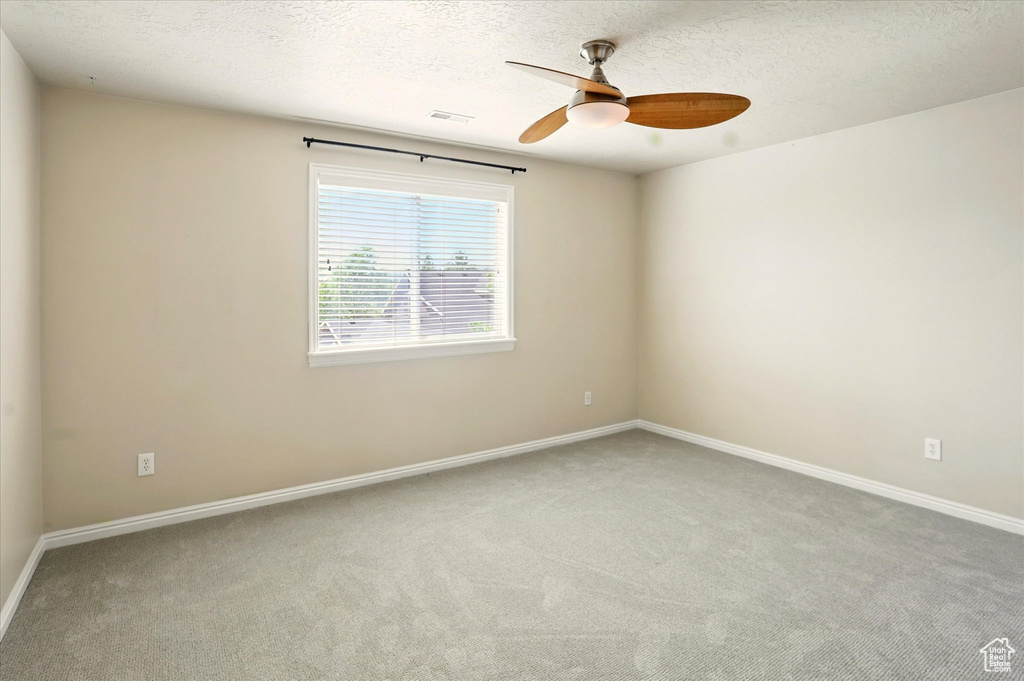 Carpeted empty room featuring a ceiling fan, baseboards, and a textured ceiling
