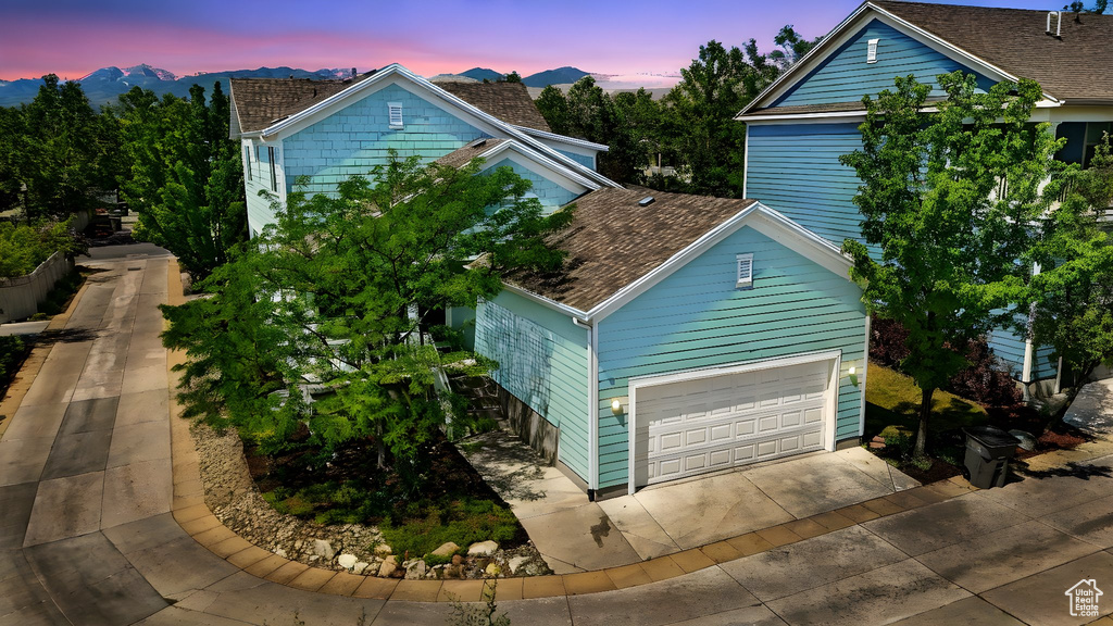 View of property exterior with driveway, a garage, a mountain view, and a shingled roof