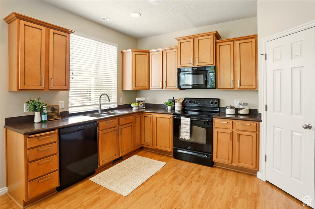 Kitchen featuring black appliances, a sink, dark countertops, light wood-style floors, and recessed lighting