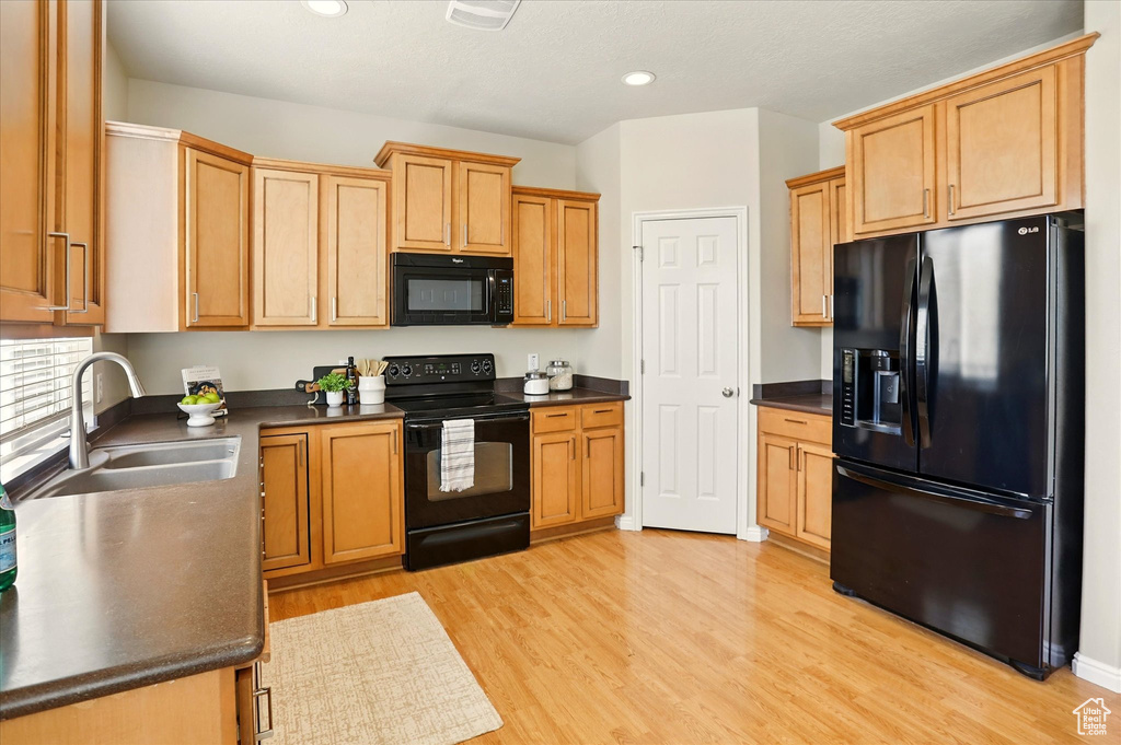 Kitchen with black appliances, a sink, dark countertops, light wood finished floors, and recessed lighting
