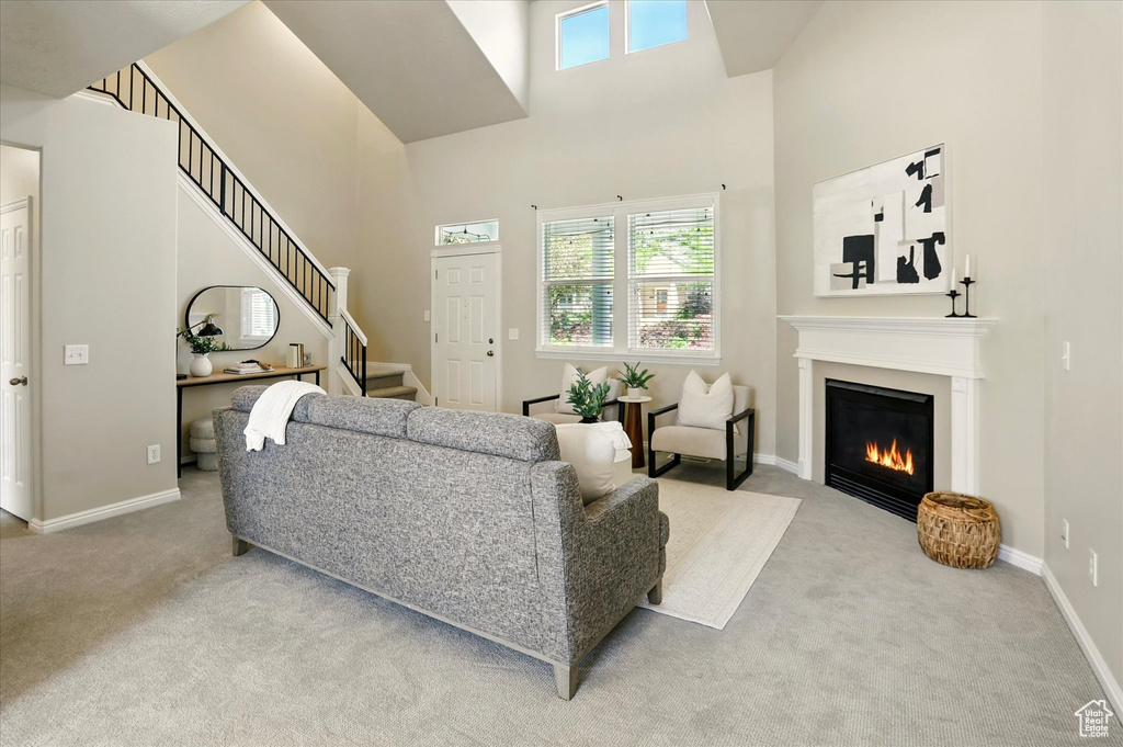 Living area featuring carpet floors, a towering ceiling, a glass covered fireplace, stairs, and baseboards