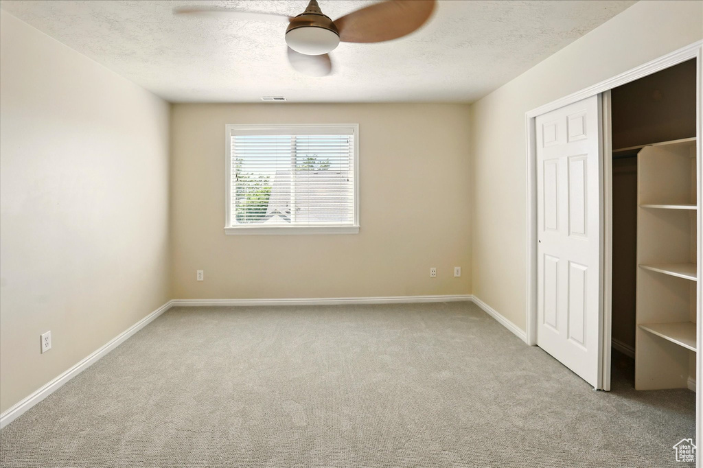 Unfurnished bedroom featuring carpet floors, baseboards, ceiling fan, a textured ceiling, and a closet