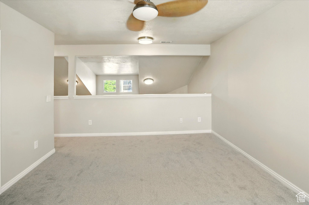 Empty room with carpet flooring, a ceiling fan, baseboards, and vaulted ceiling