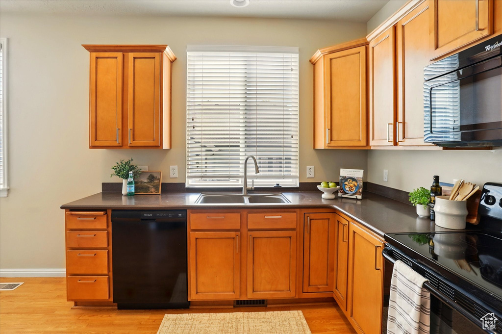 Kitchen featuring black appliances, a sink, dark countertops, and light wood finished floors