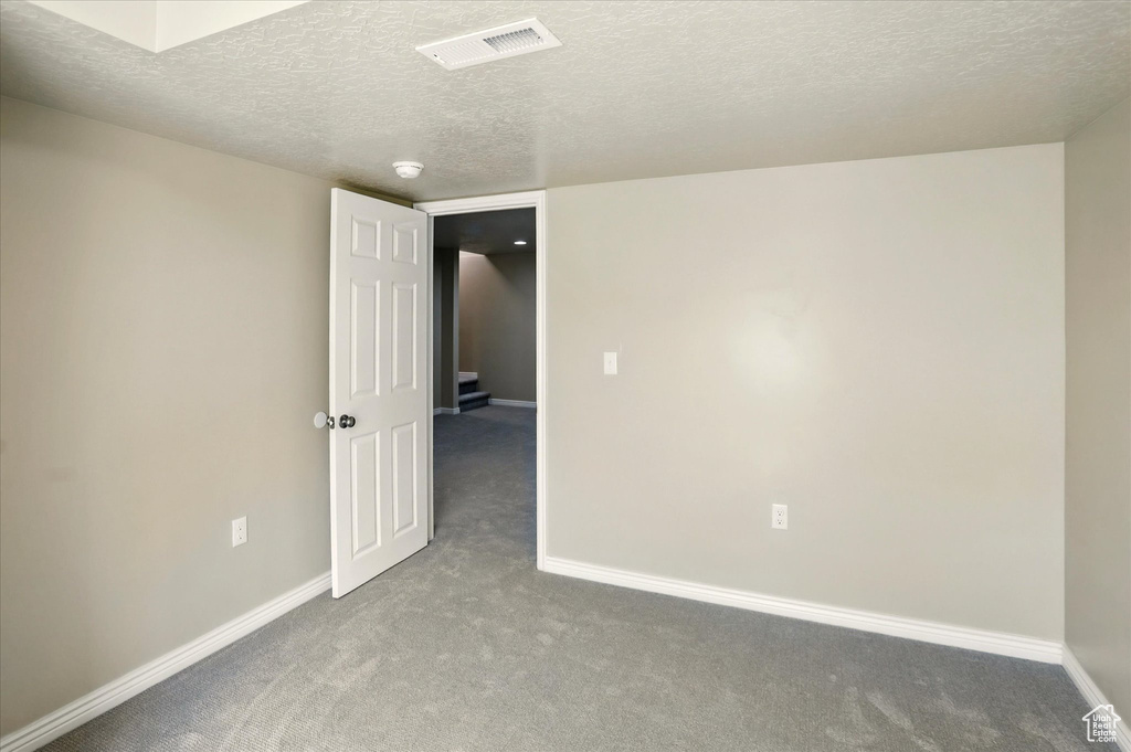 Empty room with carpet flooring, baseboards, and a textured ceiling