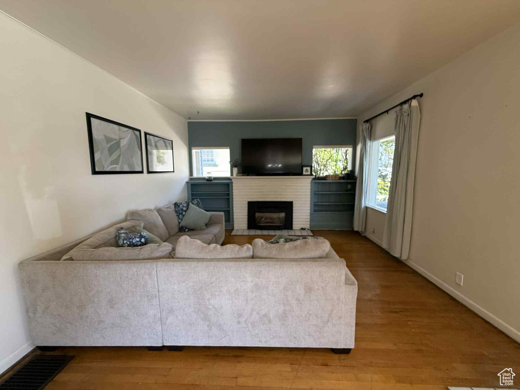 Living room with a brick fireplace, wood finished floors, and baseboards