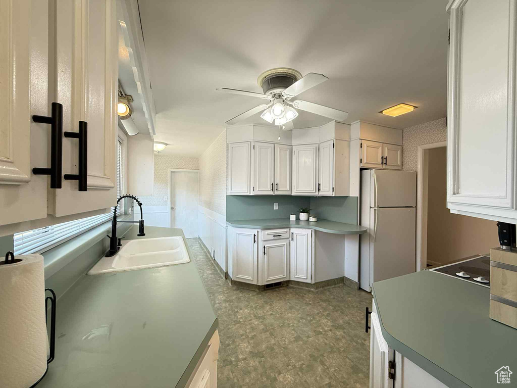 Kitchen featuring freestanding refrigerator, a sink, ceiling fan, white cabinets, and dark flooring