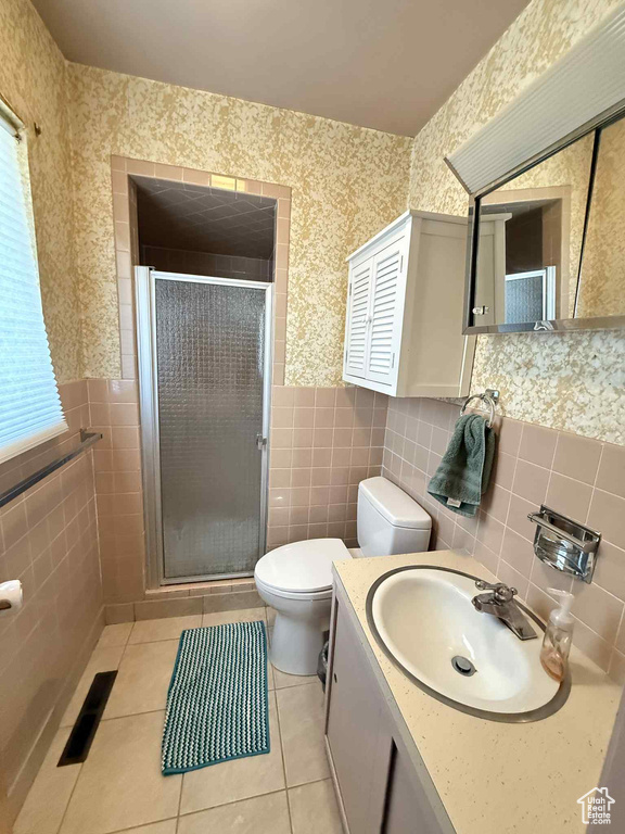 Bathroom featuring tile walls, toilet, wallpapered walls, a shower stall, and a wainscoted wall