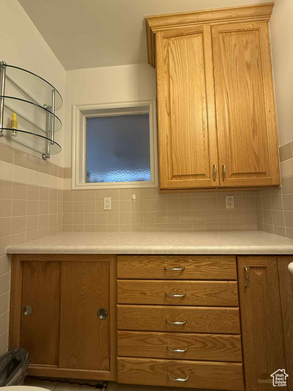 Kitchen with light countertops, tile walls, and brown cabinetry