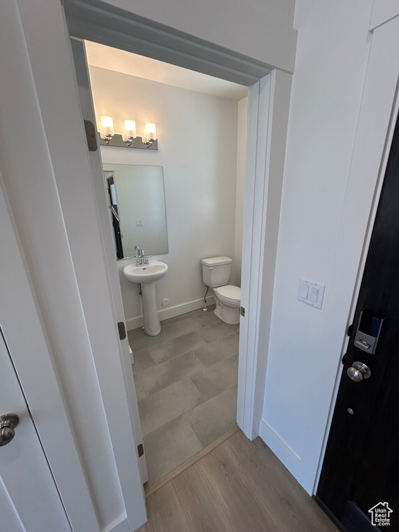 Half bathroom with toilet, baseboards, wood finished floors, and a sink