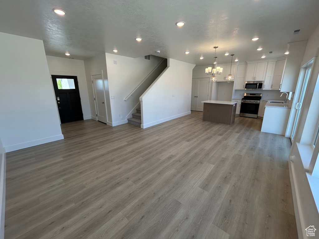 Unfurnished living room featuring a sink, baseboards, a chandelier, stairway, and recessed lighting