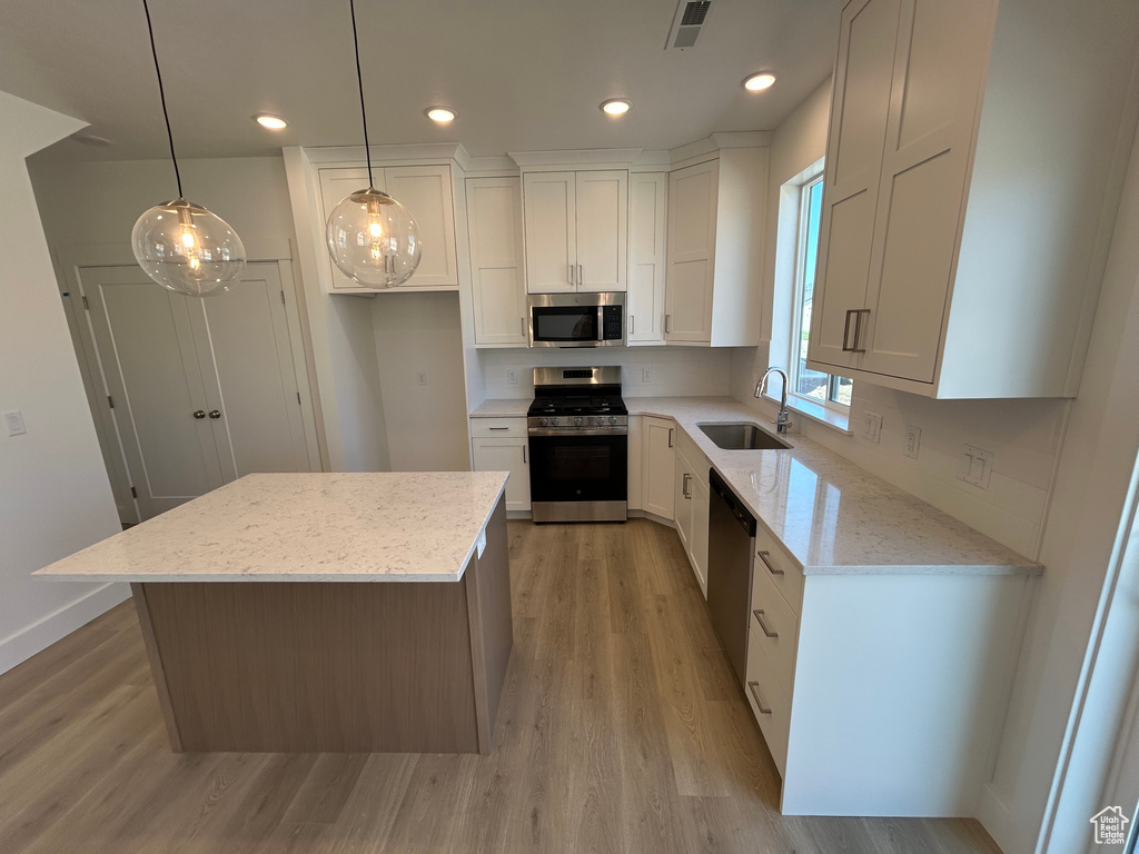 Kitchen with appliances with stainless steel finishes, a sink, light wood-type flooring, white cabinets, and recessed lighting