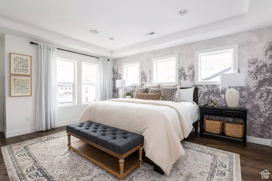 Bedroom featuring wallpapered walls, baseboards, wood finished floors, and a tray ceiling