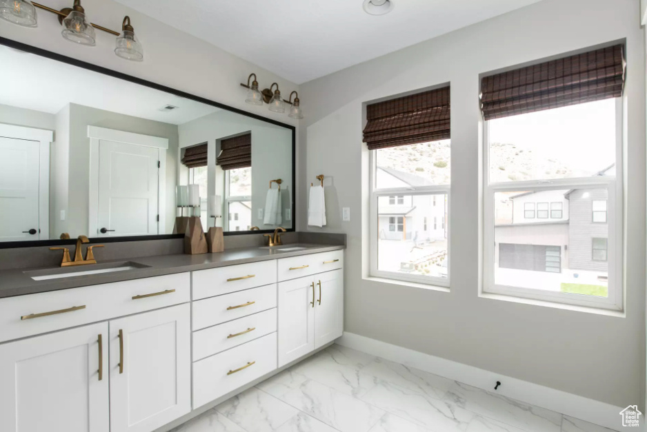 Full bath with double vanity, baseboards, marble finish floors, and healthy amount of natural light
