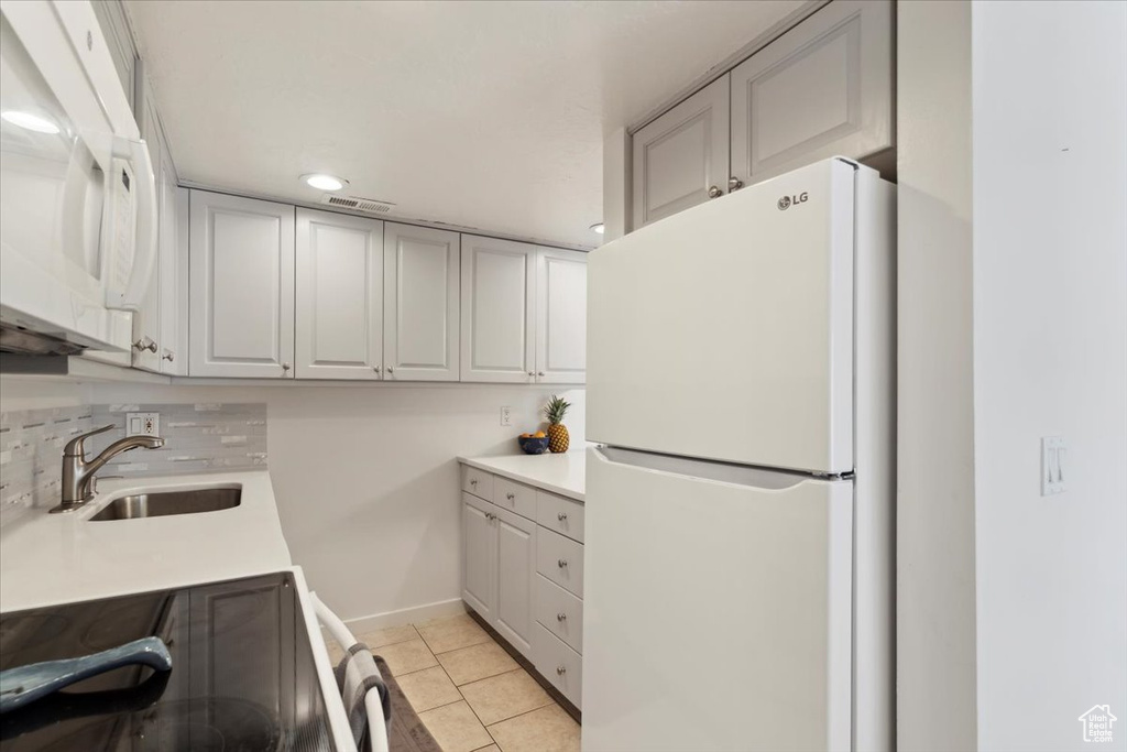 Kitchen with white appliances, a sink, decorative backsplash, and light countertops