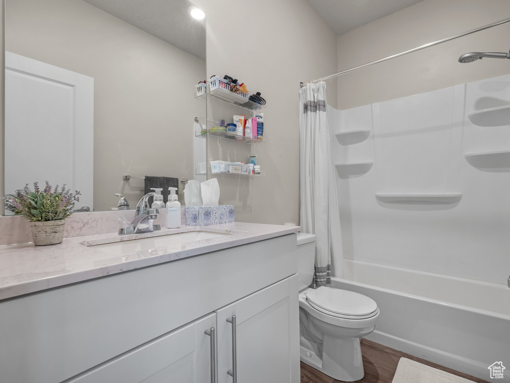 Bathroom with vanity, wood finished floors, shower / bathtub combination with curtain, and toilet