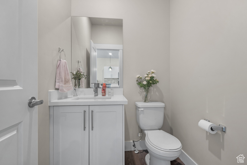 Half bathroom with wood finished floors, toilet, vanity, and baseboards