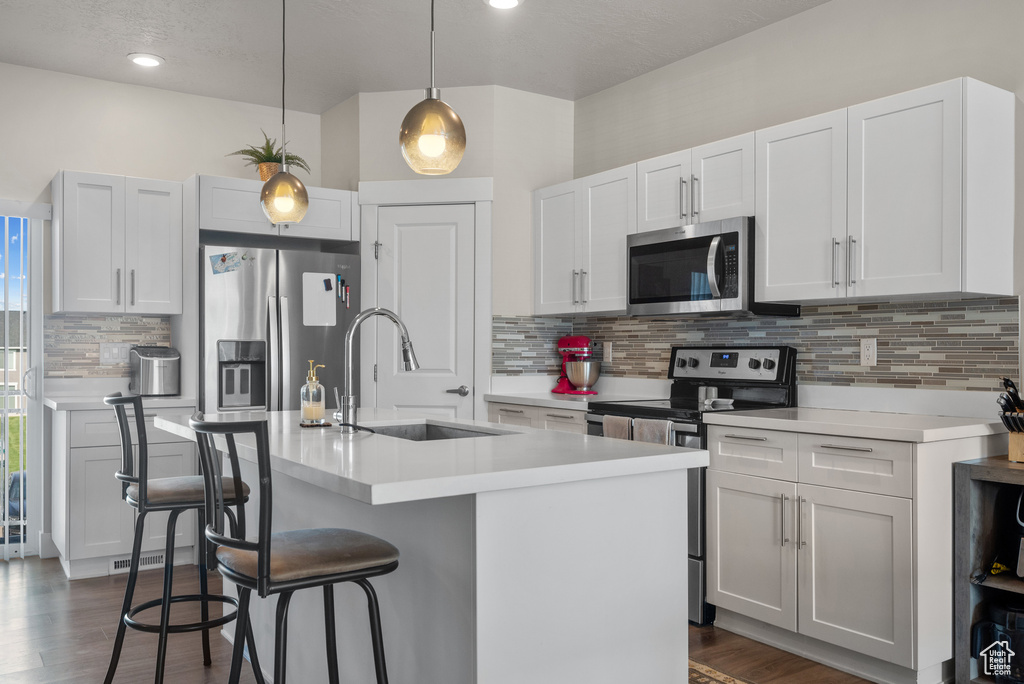 Kitchen featuring appliances with stainless steel finishes, a sink, a kitchen breakfast bar, tasteful backsplash, and light countertops