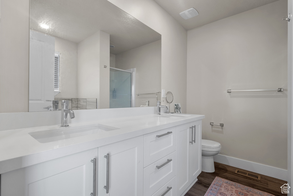 Bathroom featuring toilet, double vanity, baseboards, a shower stall, and wood finished floors