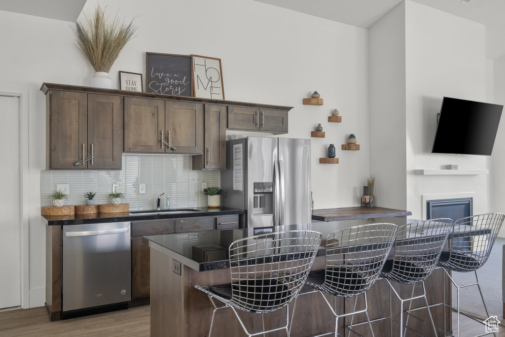 Kitchen featuring appliances with stainless steel finishes, a sink, dark countertops, a kitchen breakfast bar, and light wood-style floors