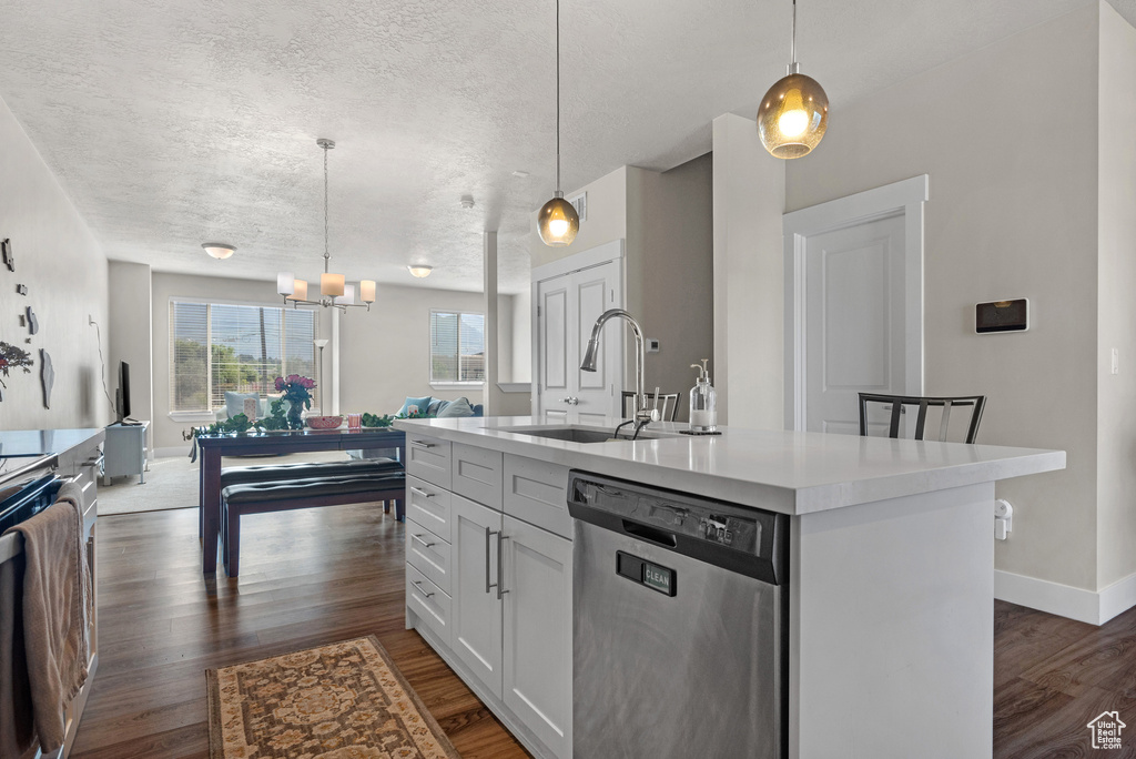 Kitchen with stainless steel dishwasher, a sink, dark wood finished floors, light countertops, and a textured ceiling