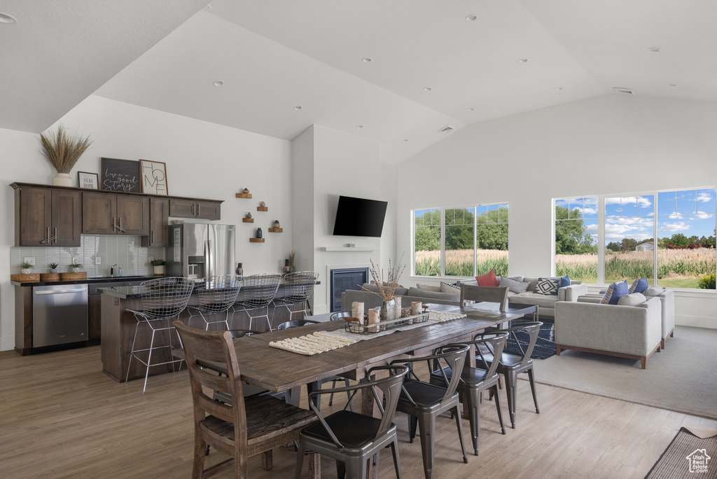 Dining room with high vaulted ceiling, light wood-style floors, and a glass covered fireplace