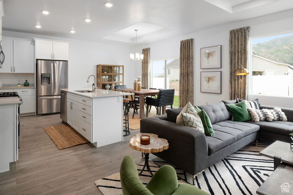 Living area with a raised ceiling, a chandelier, plenty of natural light, recessed lighting, and light wood-style floors