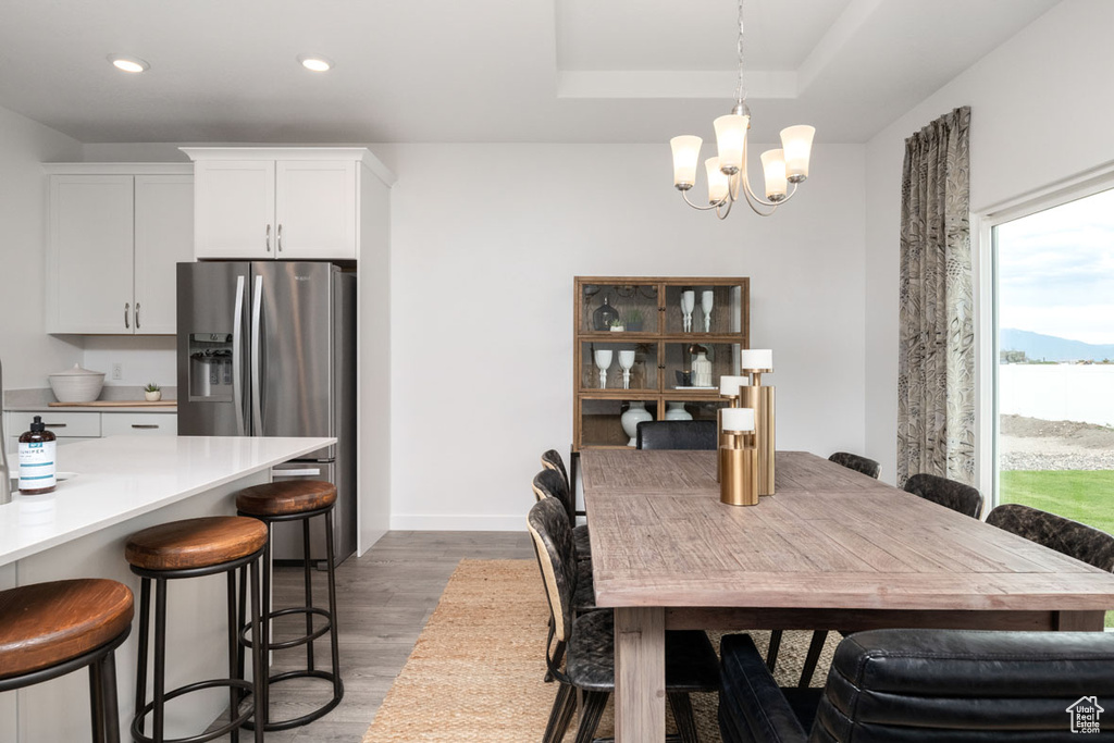 Dining room with wood finished floors, a chandelier, recessed lighting, a raised ceiling, and baseboards