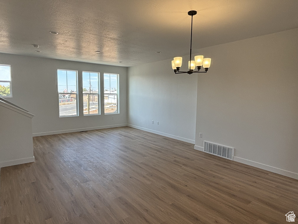 Spare room featuring wood finished floors, a chandelier, and baseboards