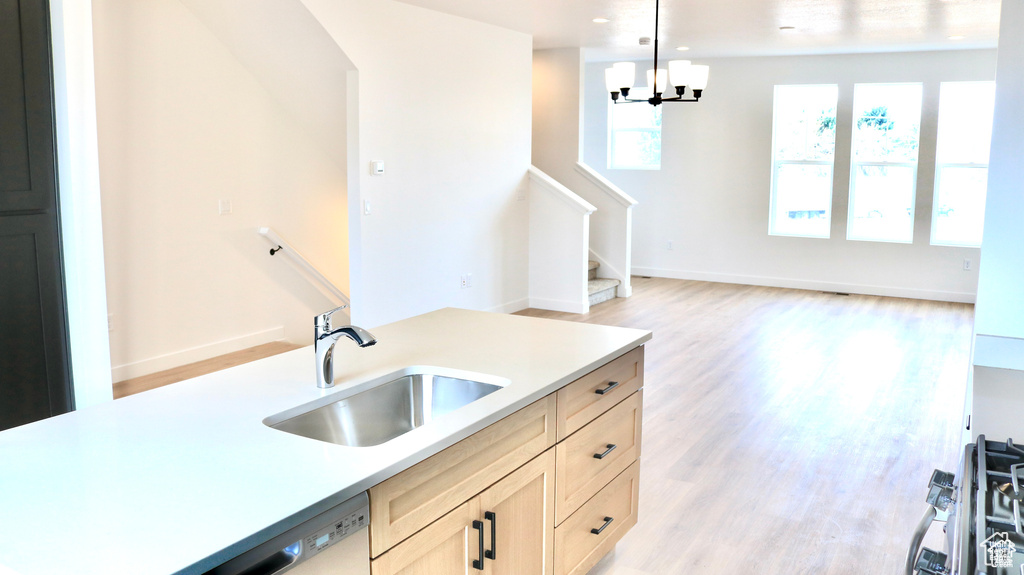 Kitchen featuring a sink, light countertops, light wood-style floors, pendant lighting, and a chandelier