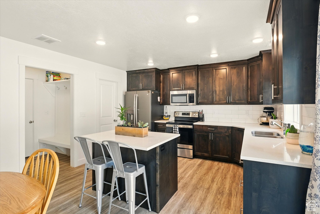 Kitchen featuring appliances with stainless steel finishes, light wood-style flooring, a sink, a breakfast bar area, and a center island