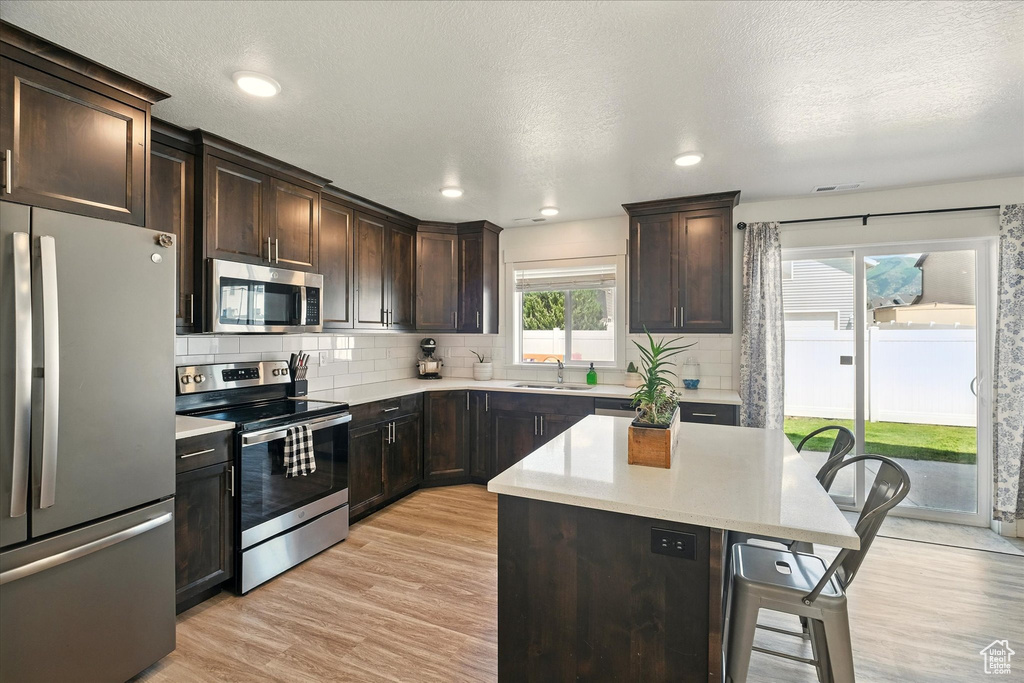Kitchen with appliances with stainless steel finishes, a sink, a kitchen breakfast bar, light countertops, and recessed lighting